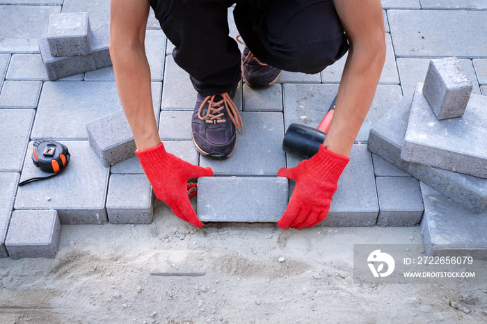 The master in yellow gloves lays paving stones