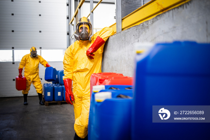 Portrait of chemical plant worker in hazmat protection suit standing by plastic containers with chemicals.