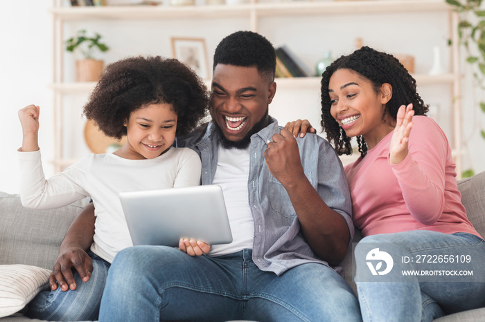 Joyful black family celebrating success with digital tablet at home