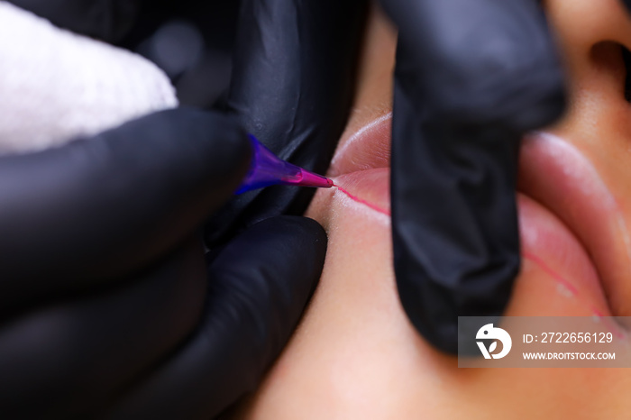 a tattoo artist in black gloves holds a tattoo machine, and the other finger presses on the client’s lips, thereby performing a lip tattoo