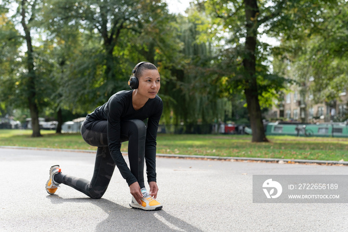 Portrait of woman in sports clothing and headphones tying shoe in park