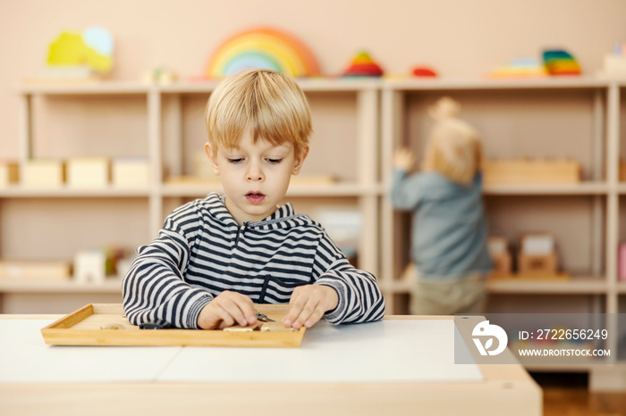 A focused child is sitting at kindergarten and learning through the game.