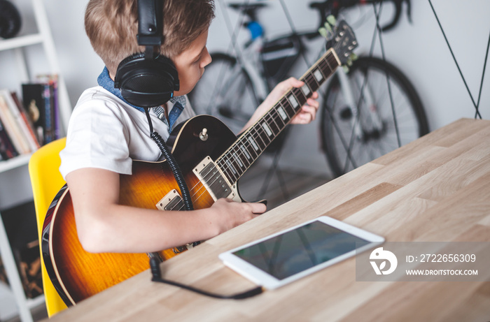 Kid boy learning to play electric guitar using tablet with headphones