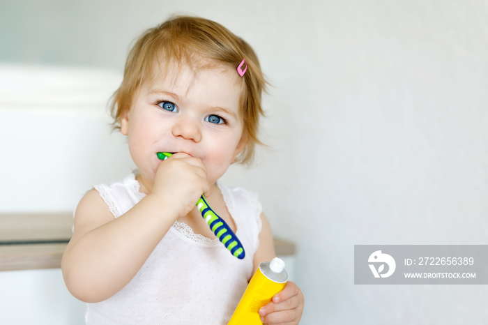 Little baby girl holding toothbrush and brushing first teeth. Toddler learning to clean milk tooth. Prevention, hygiene and healthcare concept. Happy child in bathroom