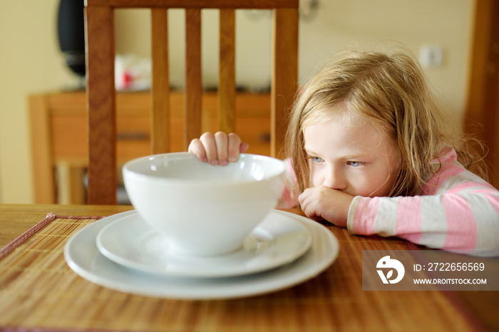 Cute little girl unwilling to eat her soup. Child having a dinner at home.