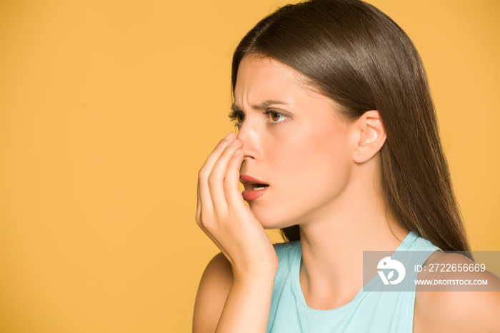 Portrait of beautiful young woman checking her breath on yellow background