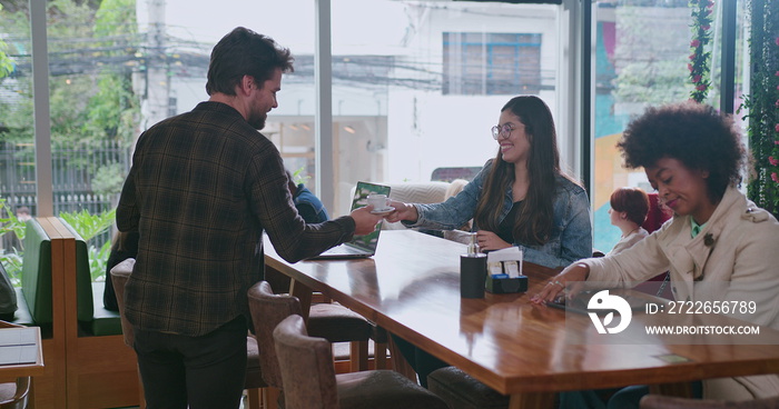 Happy male customer getting up from table and picking up two orders of espressos at coffee shop counter. Male colleague handing cafe to female colleague