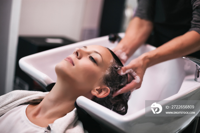 Young woman getting new hairstyle at professional hair styling saloon. Hairdresser is massaging her head.