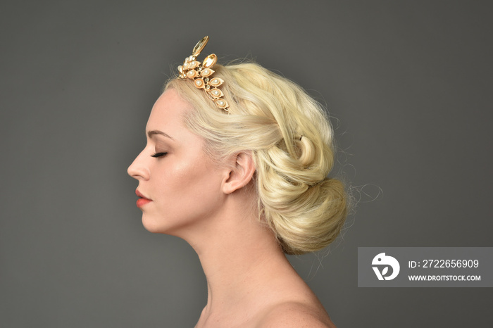 portrait of blonde woman wearing golden crown, grey studio background.