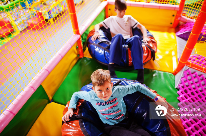 Happy two brothers in tubing donuts enjoying slides in fun children center.