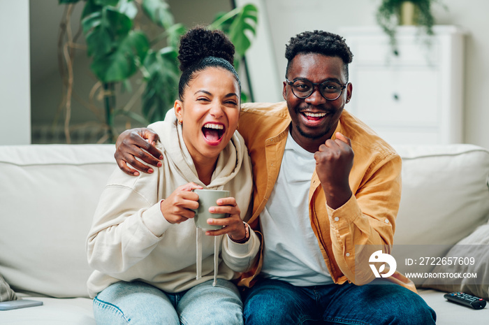 Multiracial couple watching television together at home on the couch