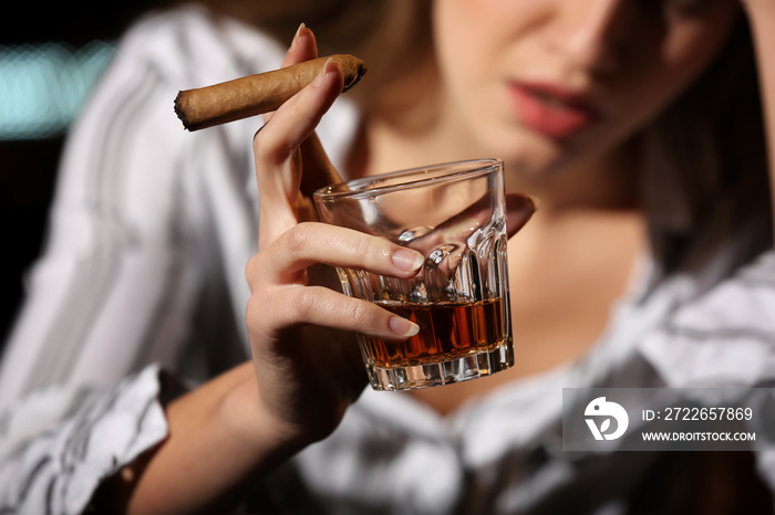 Young woman drinking alcohol and smoking cigar in bar, closeup