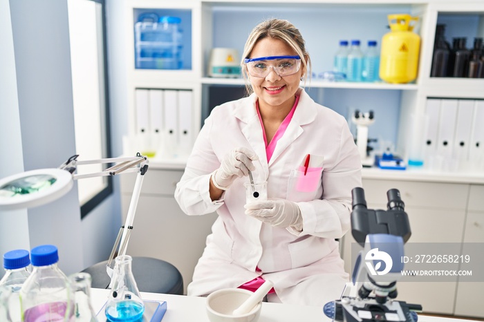 Young hispanic woman wearing scientist uniform mixing powder at laboratory