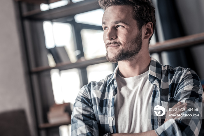 Pleasant thoughts. Joyful positive handsome man standing cross handed and smiling while having positive thoughts