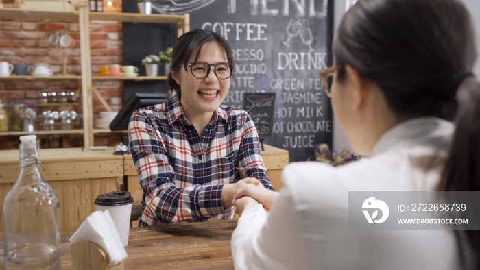 Back view of female hr shaking hand of smiling Asian job candidate in glasses. woman greeting with successful interview. lady employee handshaking supervisor making good first impression in cafe bar