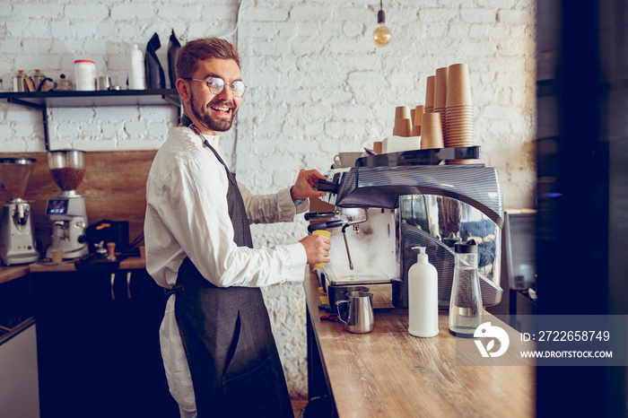 Cheerful male barista using coffee machine in cafe