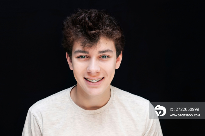 Metal braces of a young boy on the teeth, the guy is sincerely smiling on a dark background in a light T-shirt. A boy is glad that he has braces and soon teeth will be straight and healthy