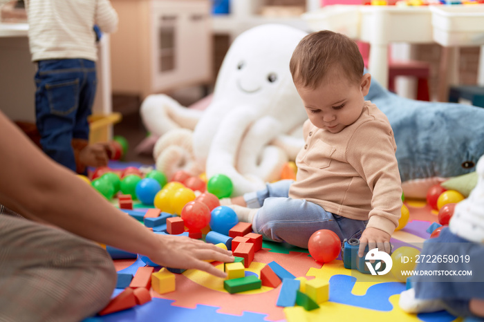 Adorable toddler playing with toys sitting on floor at kindergarten