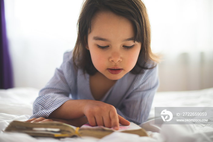 Little girl reading from bible while she is in bed in the morning