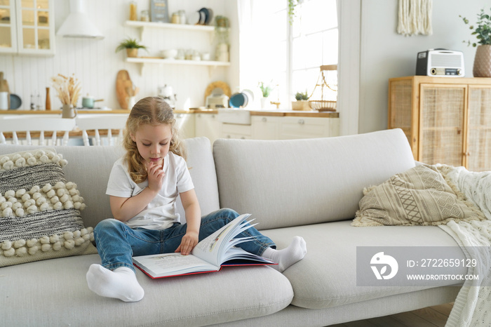 Little kid girl preschooler read fairytale book sitting on cozy couch at home alone. Child education