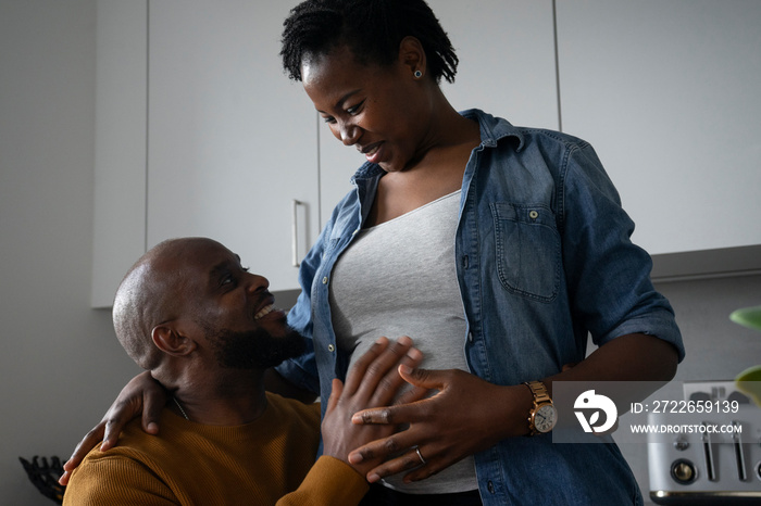 Smiling man touching pregnant woman’s belly in kitchen