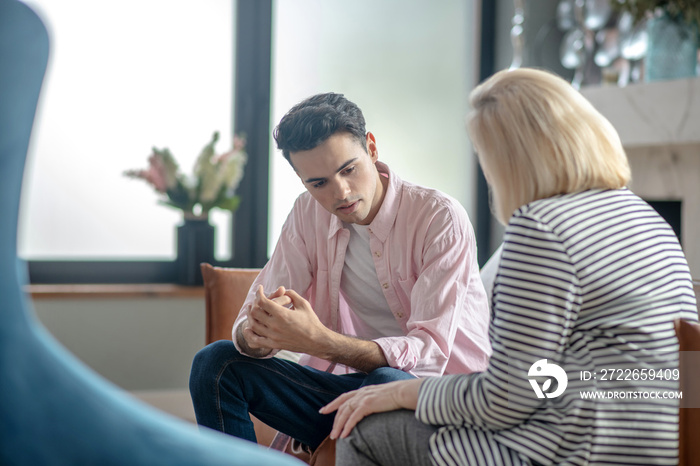 Young man in a pink shirt explaining something to psychologist