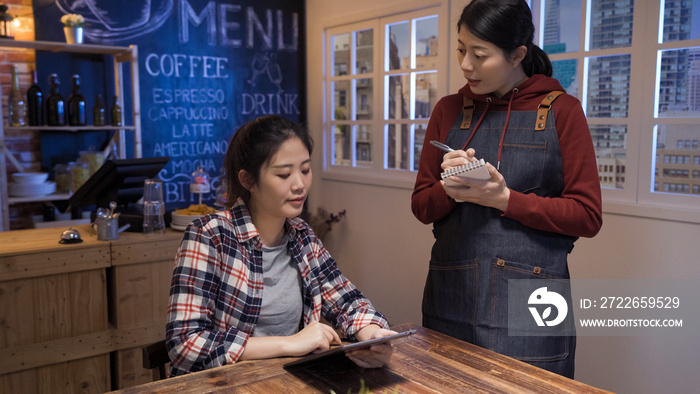 asian japanese waitress taking order on notebook in cafe restaurant. young girl customer sitting alone in night club and talking to bartender. female client holding digital tablet looking at menu.