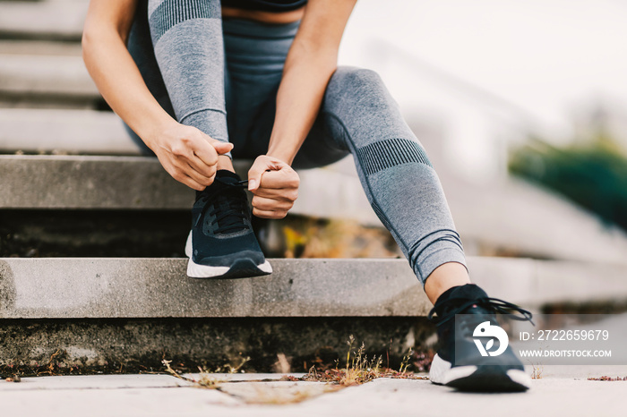 Close up of female runner sitting on the stairs outdoors and tying a shoelace on her sneaker. A runner getting ready for running