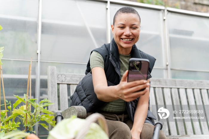 Smiling woman photographing harvested vegetables with smart phone