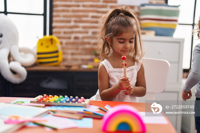 Adorable hispanic girl playing xylophone sitting on table at kindergarten