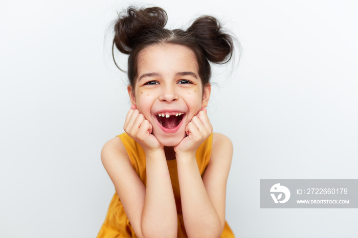 The overjoyed preschool little girl in yellow dress showing empty space with growing first permanent molar isolated on grey studio background. Happy kid missing baby tooth. A child has lost milk tooth