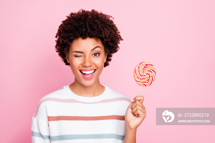 Photo of cheerful cute nice charming sweet girl holding candy with hands wearing white striped sweater blinking isolated over pastel color background