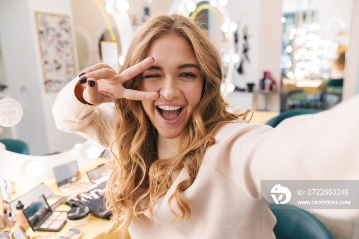 Cheery blonde girl indoors in beauty salon take a selfie