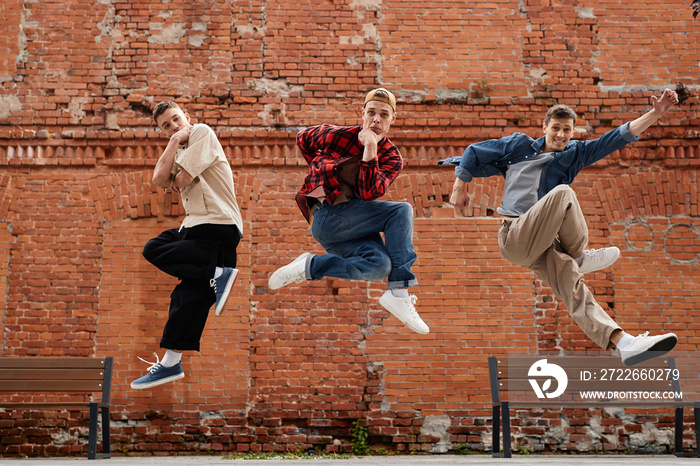 Freeze frame of all male dance team jumping in air and posing against brick wall