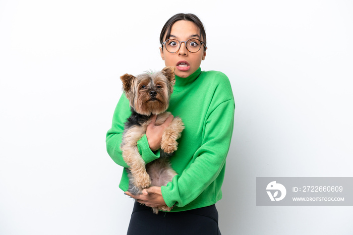 Young hispanic woman holding a dog isolated on white background with shocked facial expression