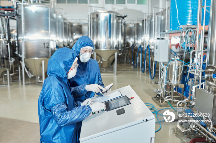 Two workers operating equipment at factory and using control panel