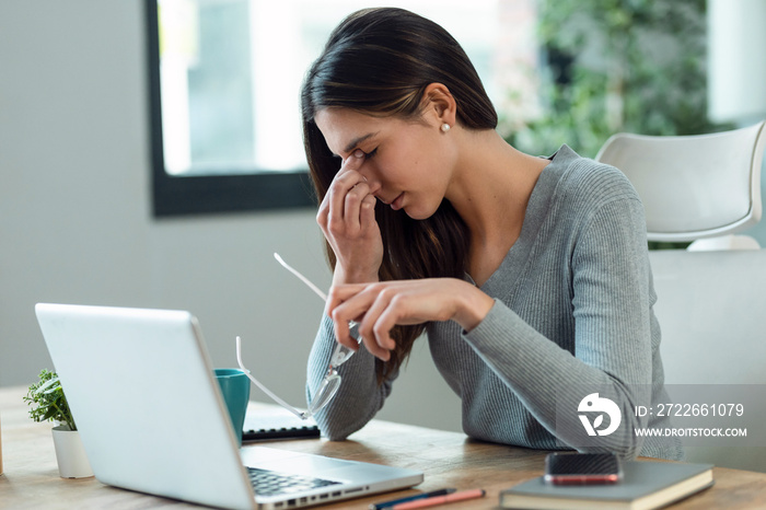 Stressed business woman working from home on laptop looking worried, tired and overwhelmed.