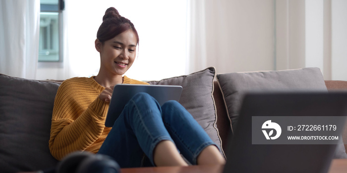 Candid of asian woman using tablet for watching online movie stream mobile device on sofa at living room. Young happy girl enjoying with entertainment media online on weekend.