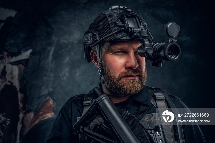 Close-up portrait of a bearded special forces soldier observes the surroundings in night vision goggles. Studio photo against a dark textured wall