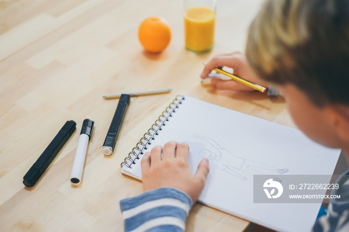 Close up view of student drawing with pencil. Boy doing homework writing on a paper. Kid hold a pencil and draw a manga at home. Teen drawing sitting at the table. Education art talent ability concept