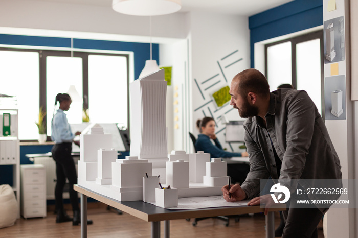 Man working on architectural design at office while looking at laptop computer for industry construction. Project manager inspecting maquette modern design building model