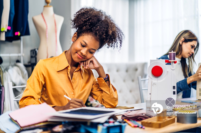 Portrait of young african american woman and young girl fashion designer stylish sitting and working with color samples.Attractive two designer girl work with colorful fabrics at fashion studio