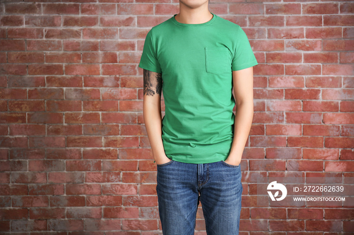 Young man in blank green t-shirt standing against brick wall, close up