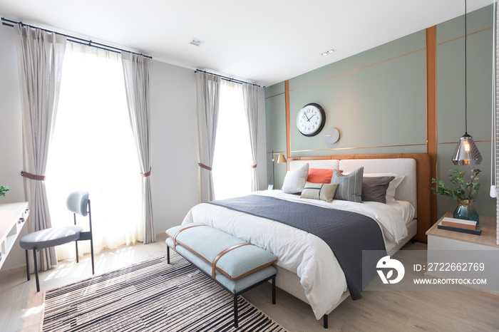 Stylish interior of modern bedroom. White, grey and pastel orange design pillow setting in cozy bedroom with clock on the wall.