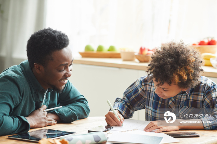 African father helping to his son to study during online education at home man explaining the material while boy making notes in notebook