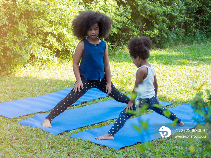 Two cute African with afro hair siblings sisters doing stretching or yoga pose on yoga mat in the garden