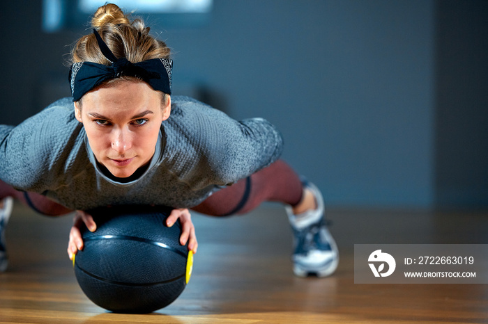 Fit and muscular woman with piercing eyes doing intense core workout with kettlebell in gym. Female exercising at crossfit gym.