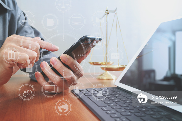 justice and law concept.Male lawyer in office with the balance brass scale,hand working with smart phone and digital tablet computer on wooden desk,virtual graphic icons screen diagram