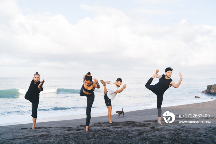 Young man and woman in sportive clothes standing in yoga pose breathing and enjoying recreation outdoors, group of diverse yogi feeling inspiration and balance in asana training at seashore beach