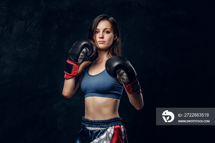 Portrait of serious female boxer in boxing gloves and sportive wear at dark photo studio.